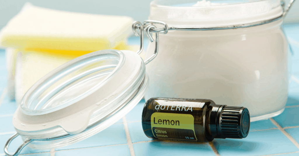 jar of diy softscrub with sponge in the background and bottle of doterra lemon essential oil