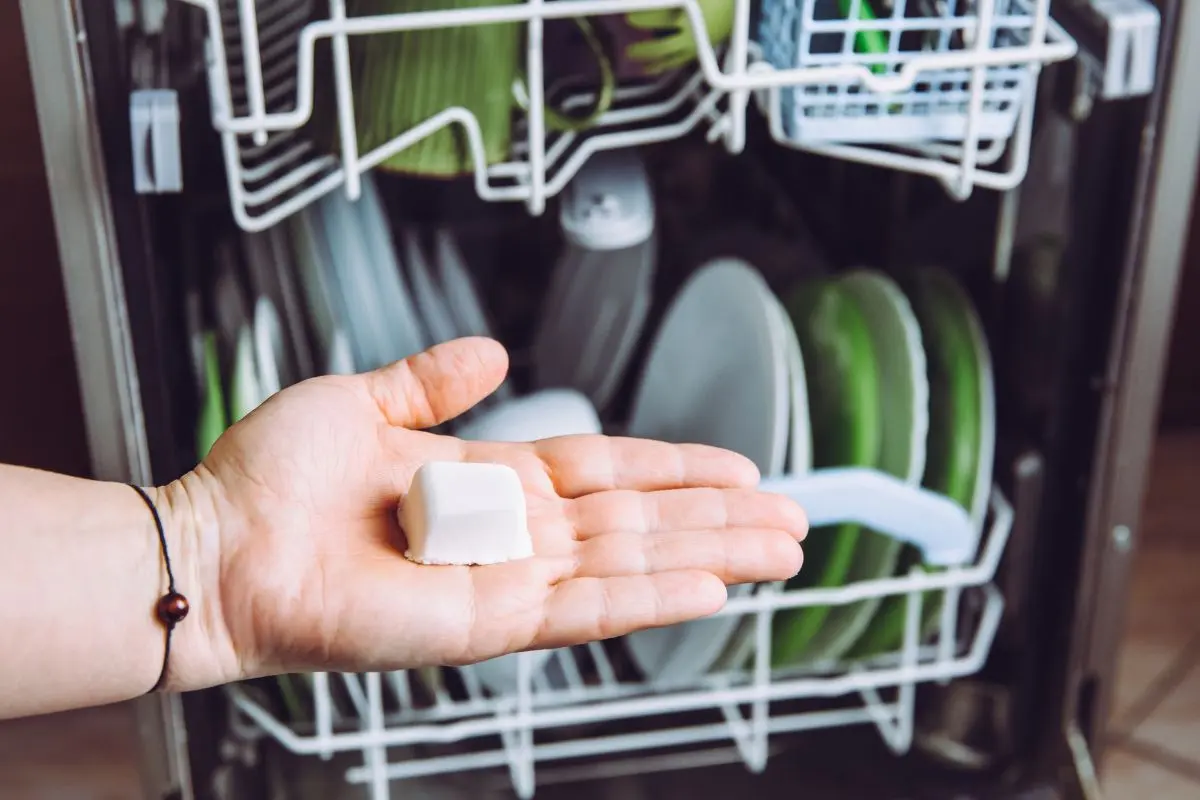 woman's hand holding a homemade diy dishwasher tablet in front of a dishwasher