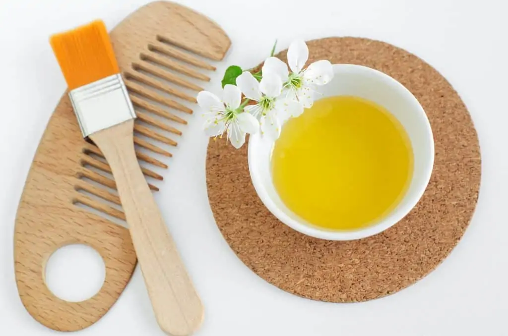 Small white bowl with cosmetic oil, white flowers, make-up brush and wooden hair brush. Natural spa and diy hair beauty treatment recipe.