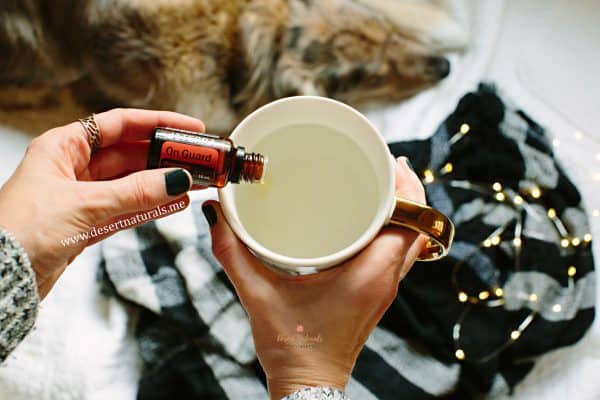 womans hands holding a mug of hot water dropping doterra on guard essential oil into the mug