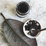 jar of homemade coffee scrub with a bowl and spoon of it on an aesthetic leaf