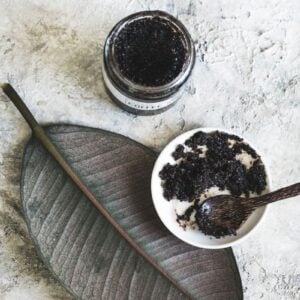 jar of homemade coffee scrub with a bowl and spoon of it on an aesthetic leaf
