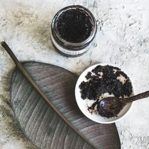 jar of homemade coffee scrub with a bowl and spoon of it on an aesthetic leaf