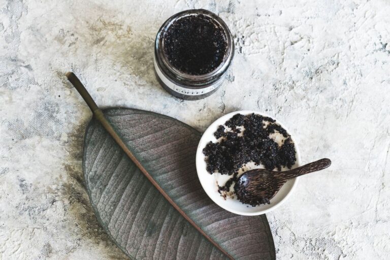 jar of homemade coffee scrub with a bowl and spoon of it on an aesthetic leaf