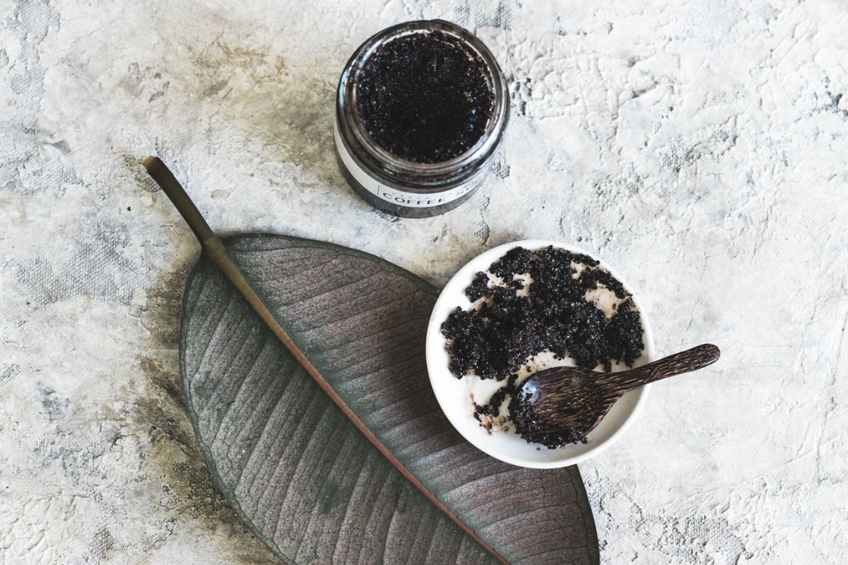 jar of homemade coffee scrub with a bowl and spoon of it on an aesthetic leaf