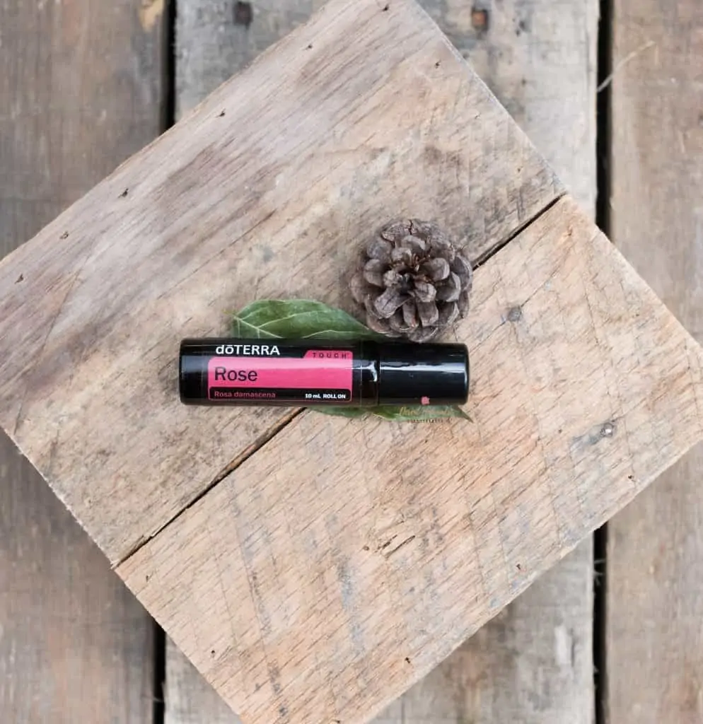 rustic wood planks with small pinecone and bottle of doterra rose essential oil roller