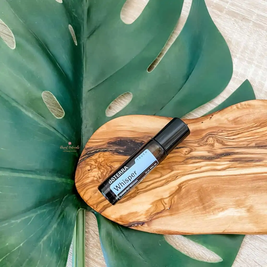 large green leaf with bottle of doterra whisper essential oil roller on a wood plank