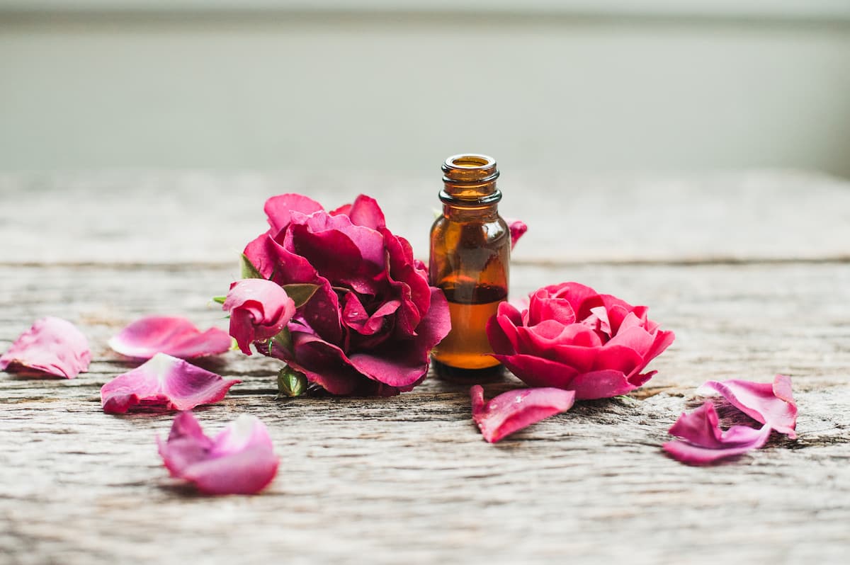 rose petals with a bottle of essential oil on wood
