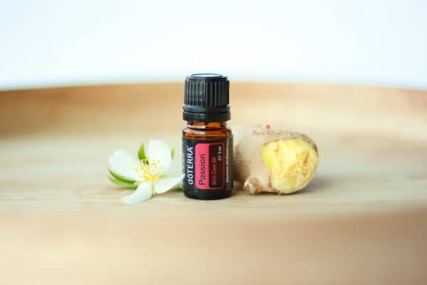 bottle of doterra passion essential oil on wooden tray with piece of ginger and a flower