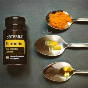 dark background with bottle of doterra turmeric capsules and three spoons showing capsules, turmeric powder and turmeric essential oil