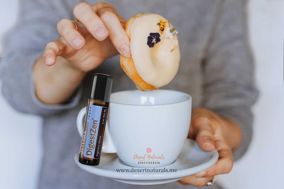 woman's hands holding coffee cup dunking a donut and a doterra digestzen touch roller next to it
