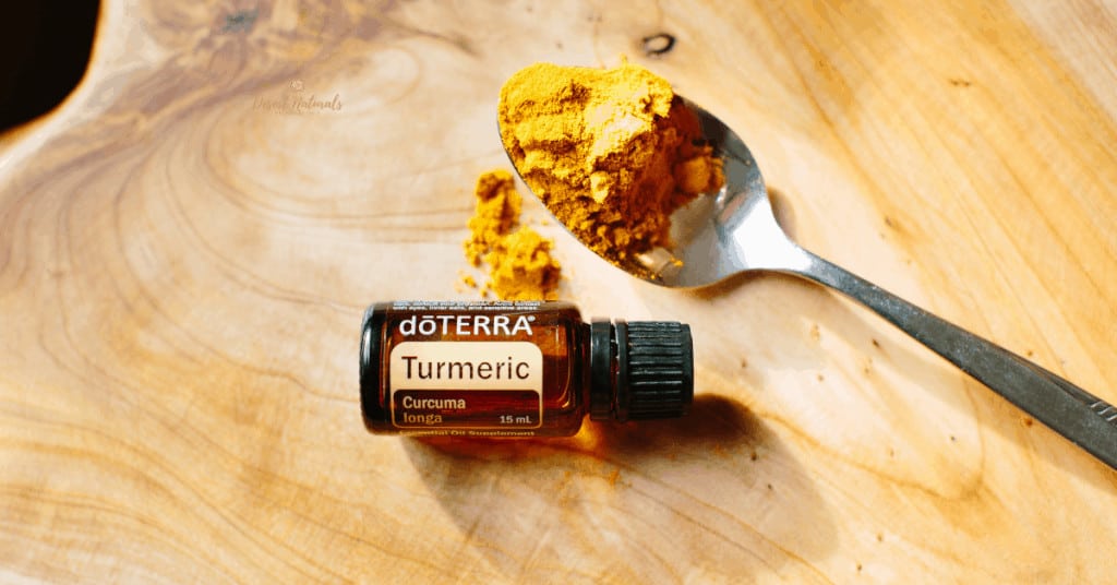spoon with dried turmeric powder and bottle of doterra turmeric essential oil