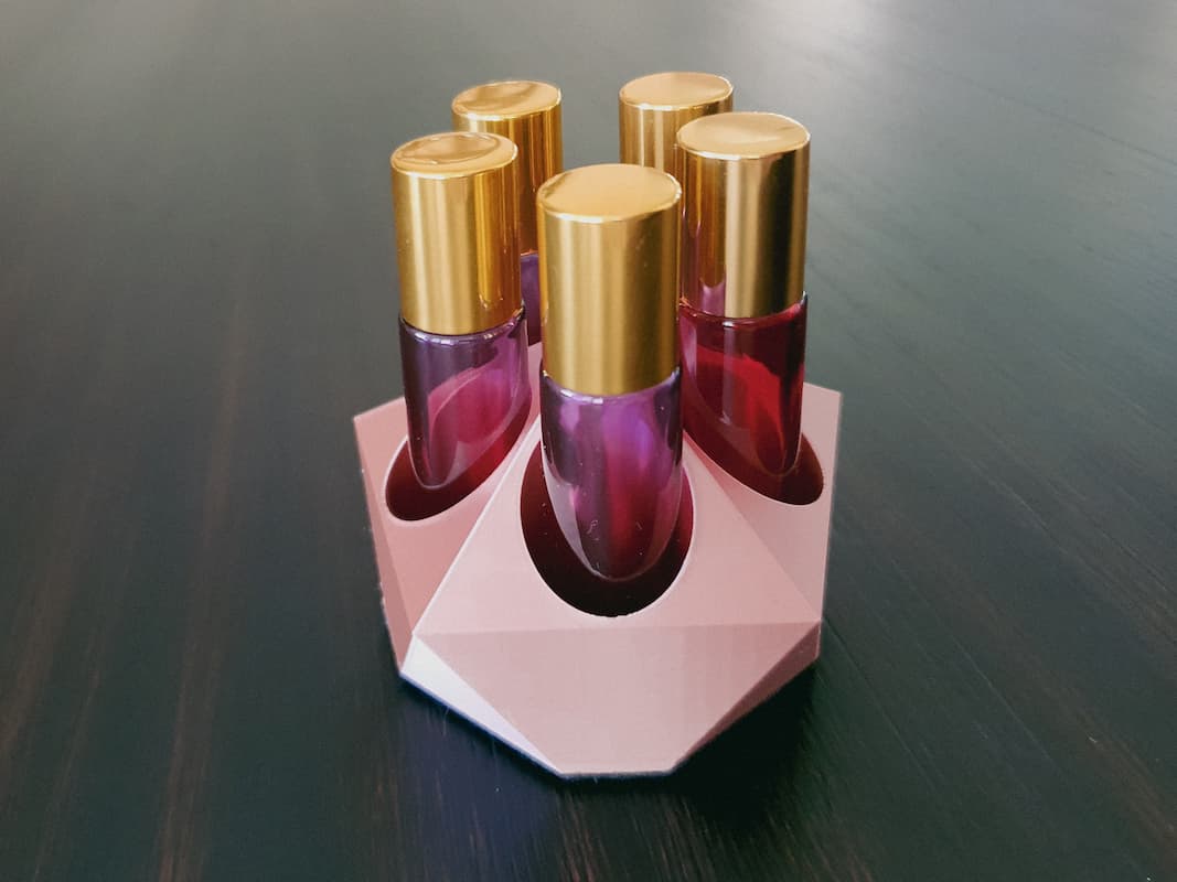 rose gold essential oil roller holder with pink and gold rollerballs on black table