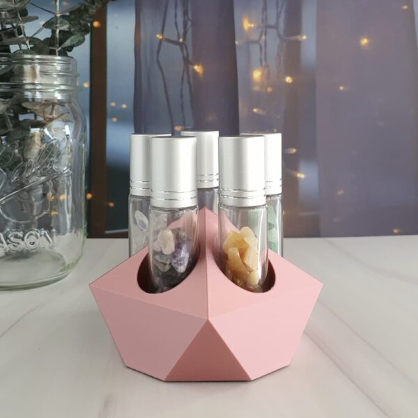 rose gold essential oil roller holder with crystal rollers on counter in front of fairy lights