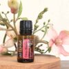 bottle of doTERRA citrus bloom on a wooden pedestal with pink flowers in the background