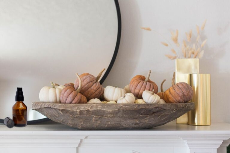 fireplace mantel with a wooden bowl of fall pumpkins and a small glass essential oil spray bottle next to it