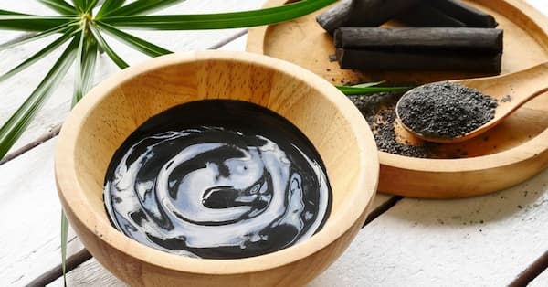 wooden bowls containing activated charcoal mixed with water and a green plant in background