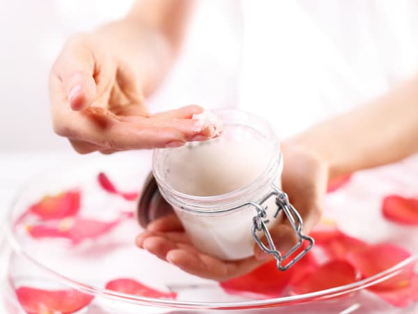 rose petals and a woman's hand scooping out some diy rose salt scrub from a jar