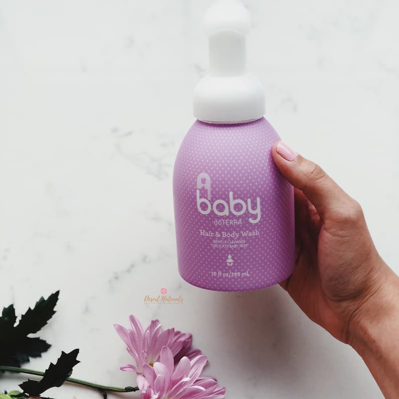woman's hand holding doTERRA baby hair shampoo and body wash with flowers