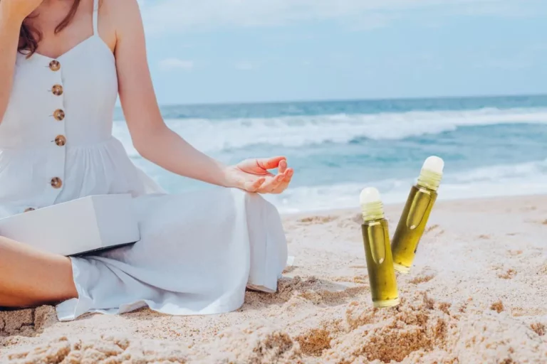 woman relaxing on beach in the summer with essential oil roller bottles