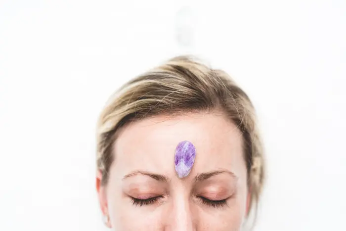 woman with amethyst crystal placed on her third eye chakra 