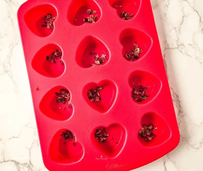 dried rose petals in the bottom of a heart shaped silicone mold for diy romance shower steamers.