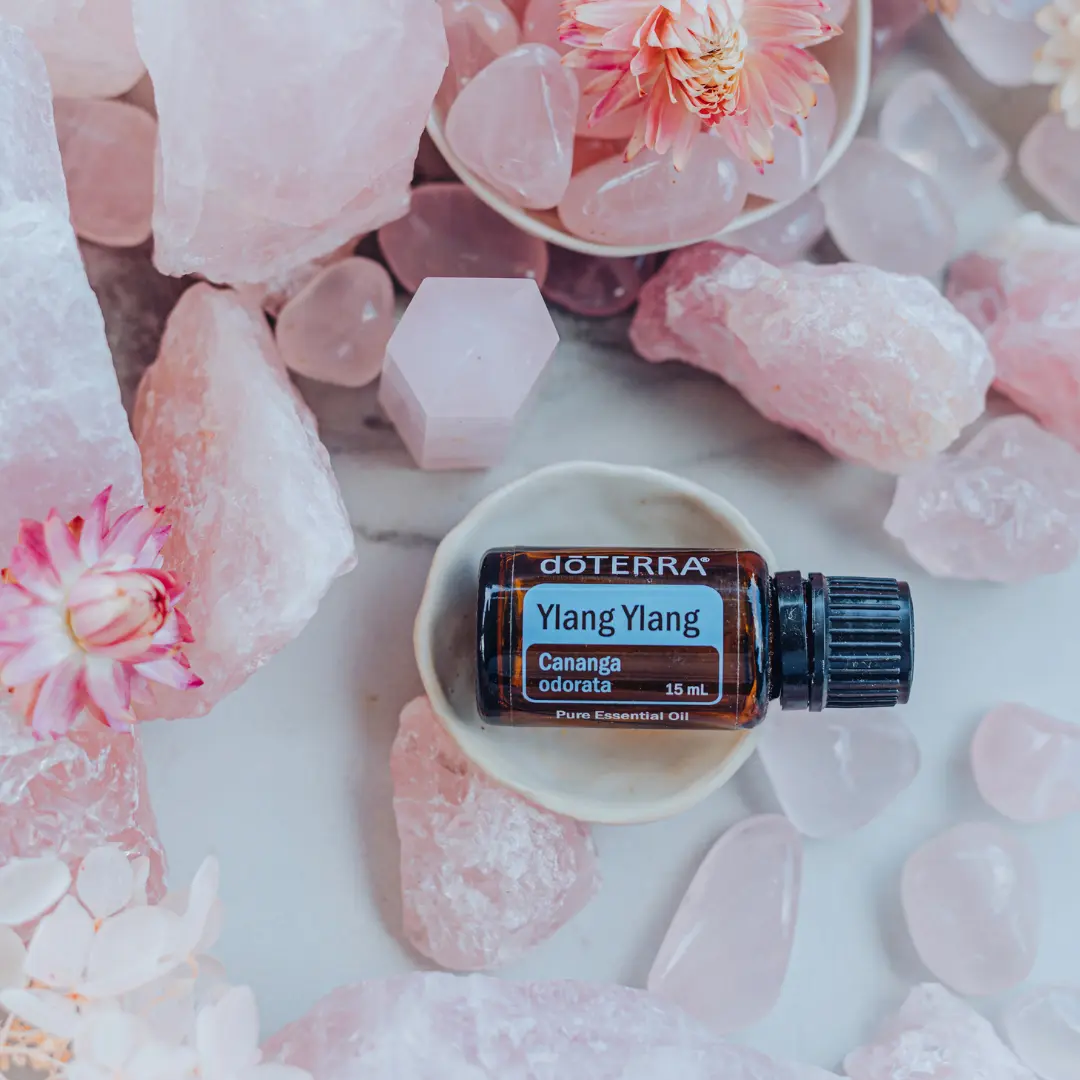 bottle of doterra ylang ylang essential oil surrounded by pink crystals