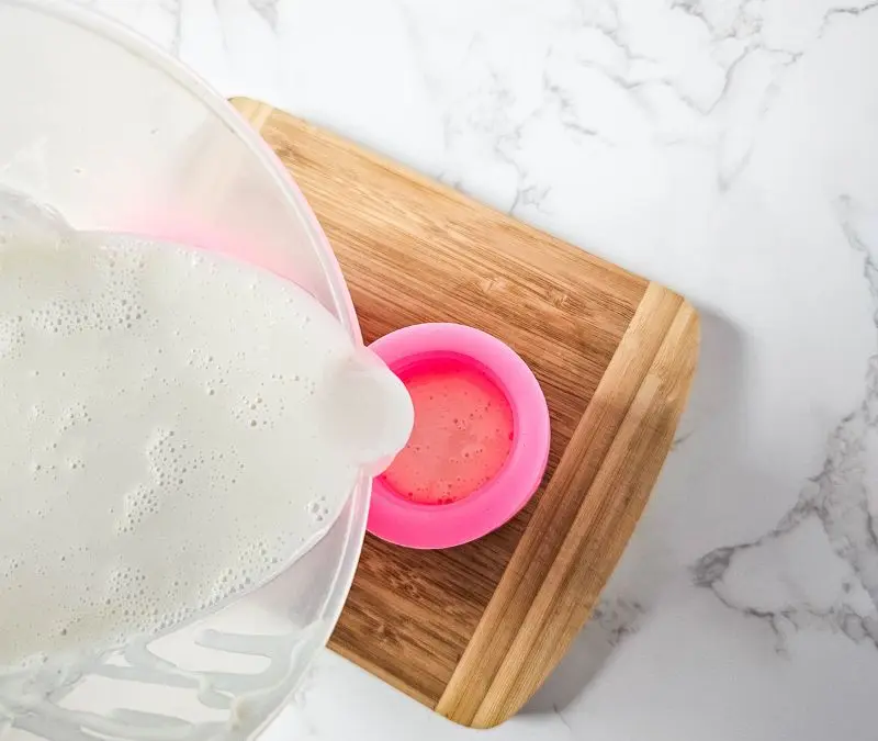 pouring melted soap base into a silicone mold to make soap bars.