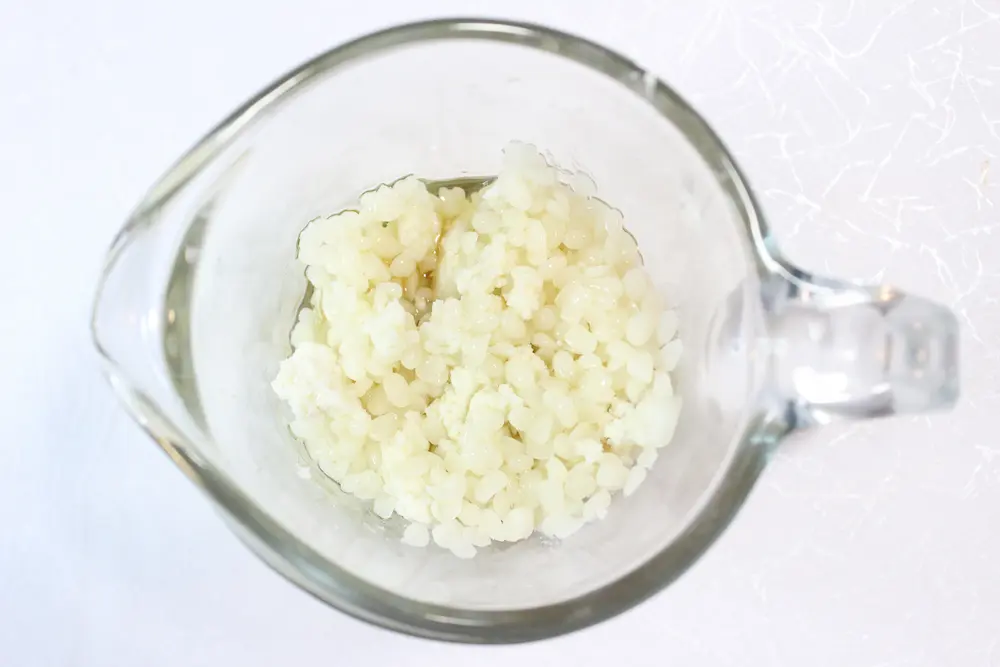 melting beeswax and other ingredients in a glass bowl to make homemade lilac lotion