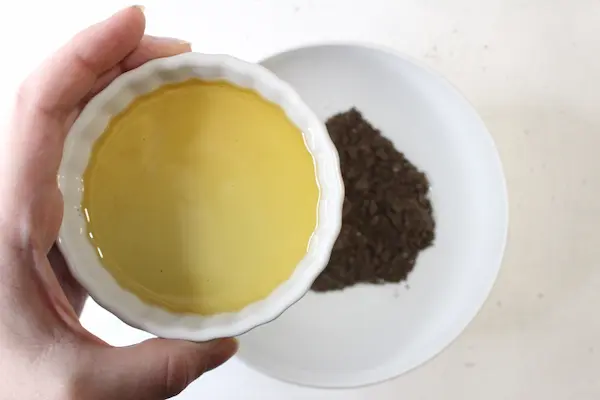 a person holding a bowl of carrier oil pouring into coffee oatmeal scrub