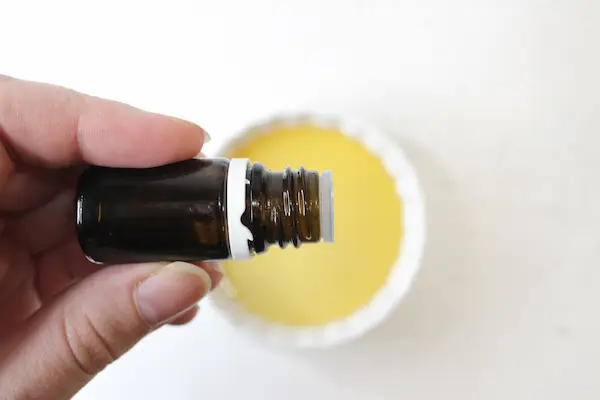 a hand holding a small bottle of essential oil adding drops to carrier oil