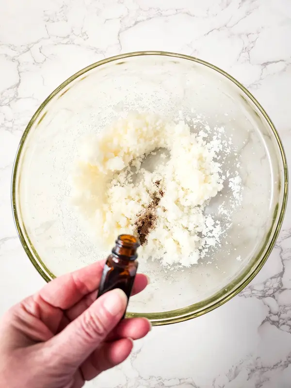 photo of adding essential oil to a glass bowl with ingredients in it for lemon vanilla sugar scrub
