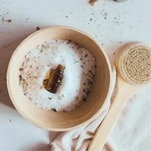 photo of epsom salts in a bowl with a bottle of essential oil and a dry brush