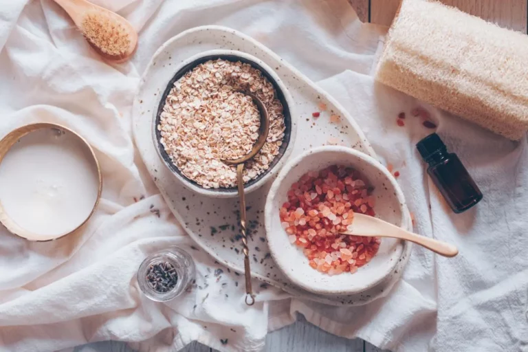 a bowl of oatmeal, milk, essential oil and pink salt on a white towel for making a lavender milk bath