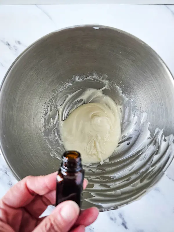 bowl of homemade magnesium lotion with a hand adding drops of essential oil