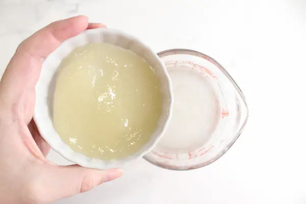 measuring cup of melted soap base and hand holding cup of sea moss gel .