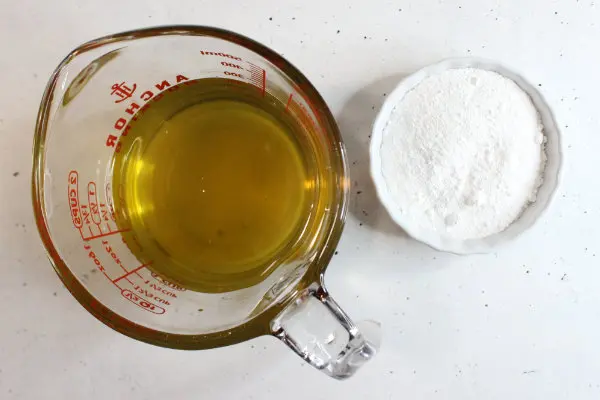 glass measuring cup with melted oils and butters with a bowl of zin oxide next to it for making homemade sunscreen