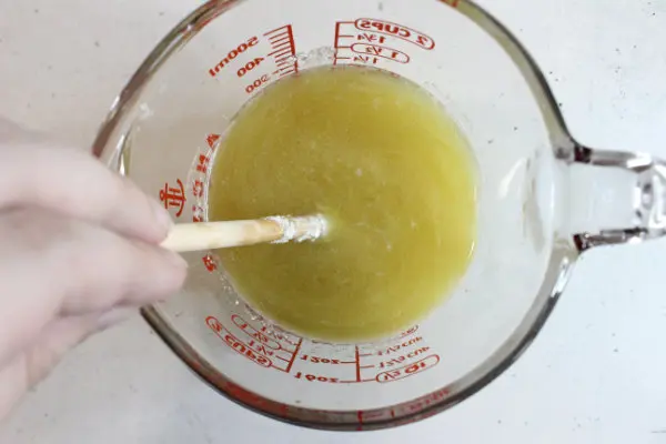 glass measuring cup with melted oils and butters and zinc oxide in it for making diy sunscreen