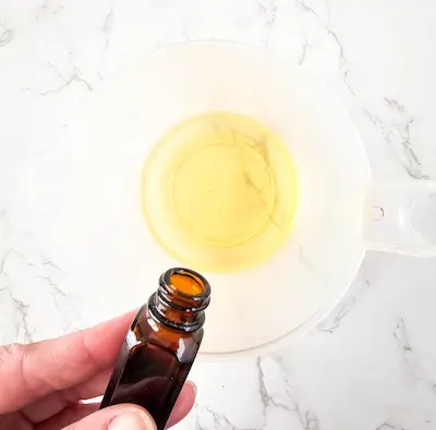 a hand adding essential oil to melted butters for making lotion bars