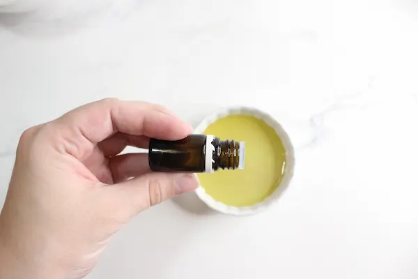 a bowl of jojoba oil and a woman's hand adding essential oil to it
