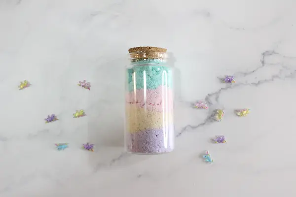 a glass jar with rainbow colored bath salts layered in it