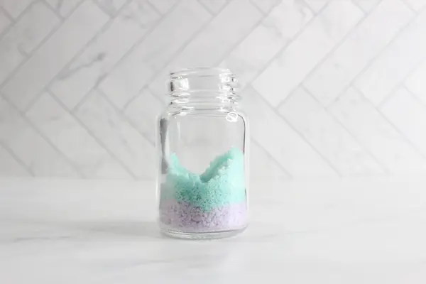a clear glass jar with purple and green bath salts layered in it