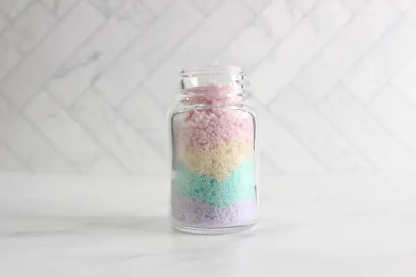 a clear glass jar with pink, yellow, purple and green bath salts layered in it