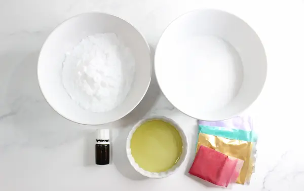 bowls of oils and salts needed to make diy rainbow bath salts body scrub