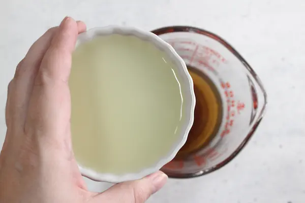 a cup of lemon juice being added to a measuring cup of chamomile lavender tea to make sleep gummies