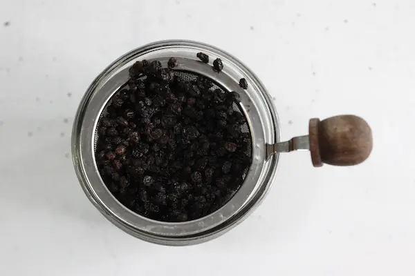 a mason jar with a strainer full of elderberries