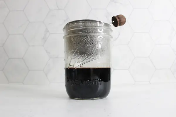 a mason jar with a strainer full of elderberries