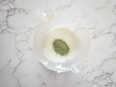 a measuring cup with a melt and pour soap base mixture and green tea leaves
