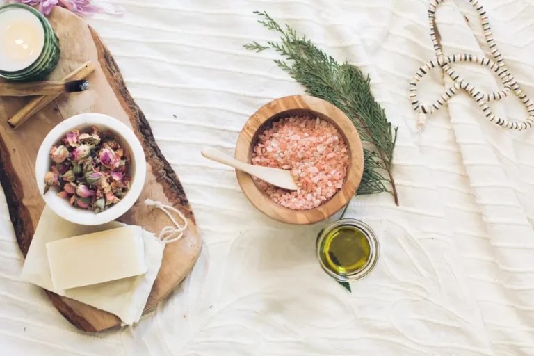 image of a wooden bowl filled with bath salts, a wood plank with dried rose hips and a candle