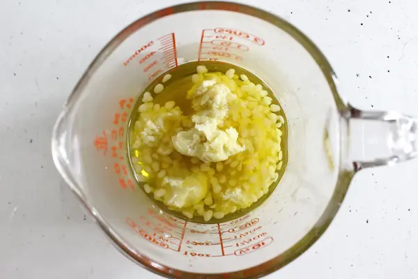 a glass measuring cup with unmelted beeswax, shea butter and oil for making diaper rash cream.